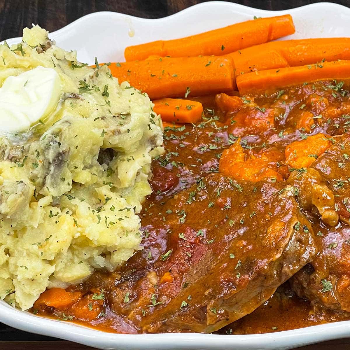 swiss steak on a platter with mashed potatoes and carrots