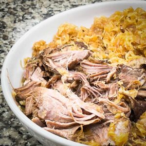 pork and sauerkraut in a large serving bowl with tongs