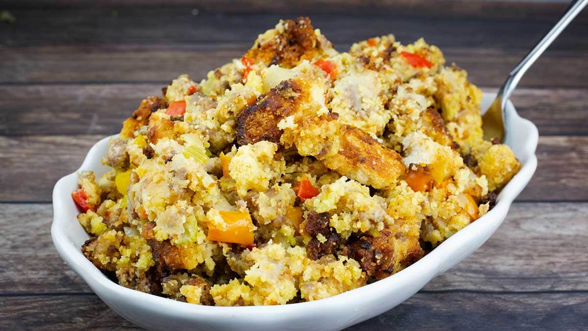 sausage and cornbread stuffing in a white serving bowl with spoon
