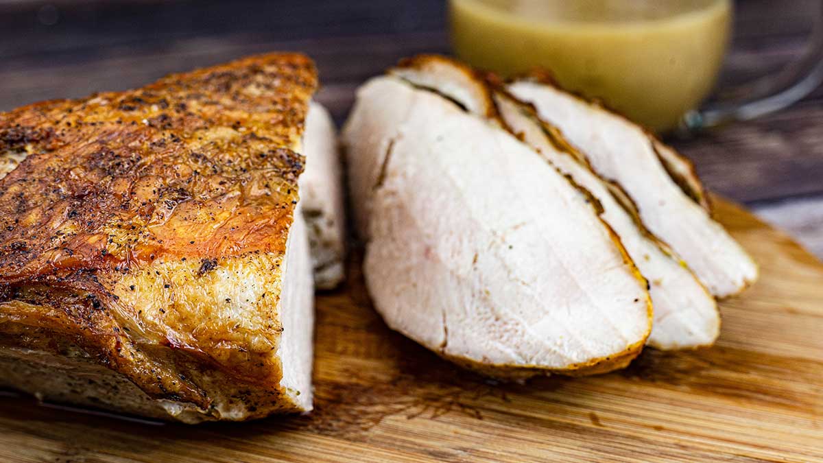 Sous Vide Turkey Breast with crispy skin on cutting board with 4 slices and gravy in the background