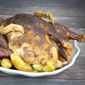 Whole duck with potatoes sitting on a white platter