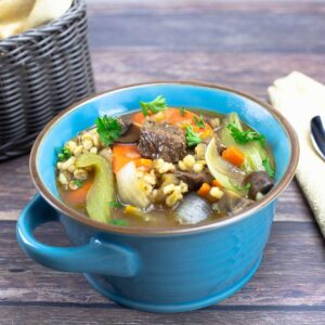 beef and barley soup in a blue bowl next to a gold napkin with a spoon