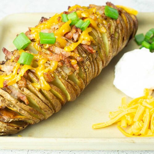 Hasselback potato with cheese, bacon, green onions on top and sour cream green onions and cheese on the side.