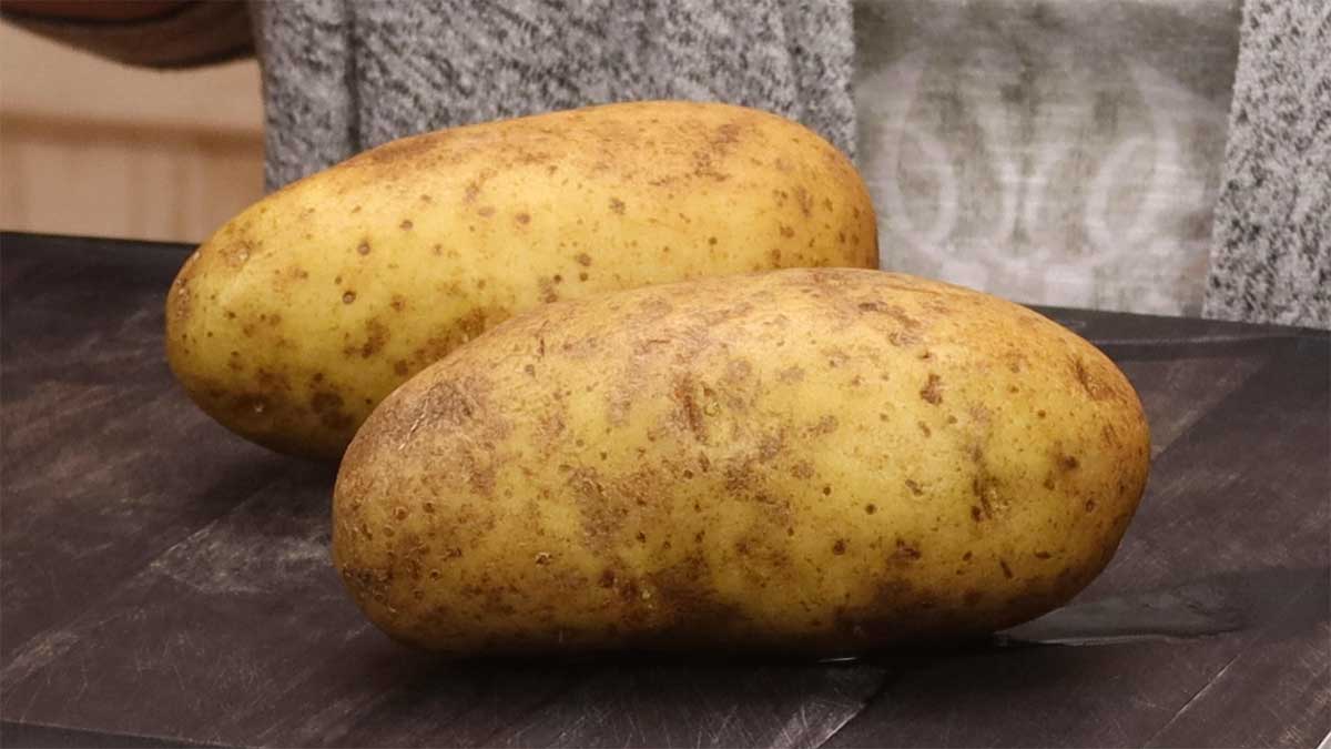 two medium size potatoes on cutting board.