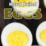 Hard boiled eggs cut in half sitting on a wood cutting board showing perfectly cooked whites and creamy yolks