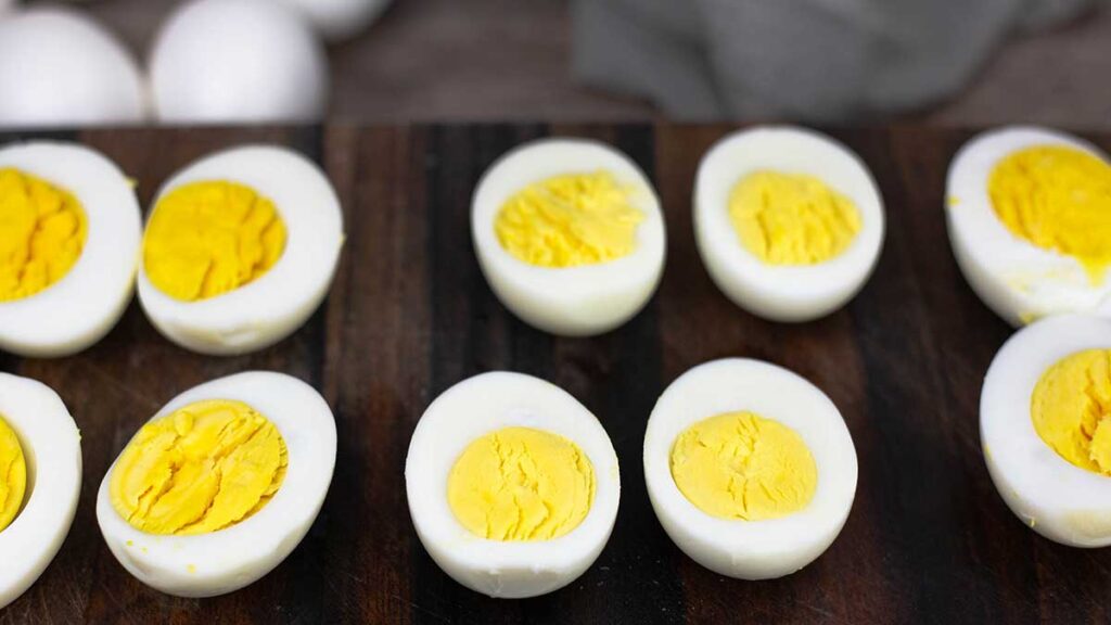 Hard boiled eggs cut in half sitting on a wood cutting board showing perfectly cooked whites and creamy yolks