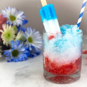 bomb pop cocktail in glass with red white and blue flowers to the left