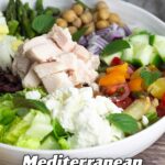 mediterranean salad in white bowl with a lemon and a bottle of lemon dressing beside it