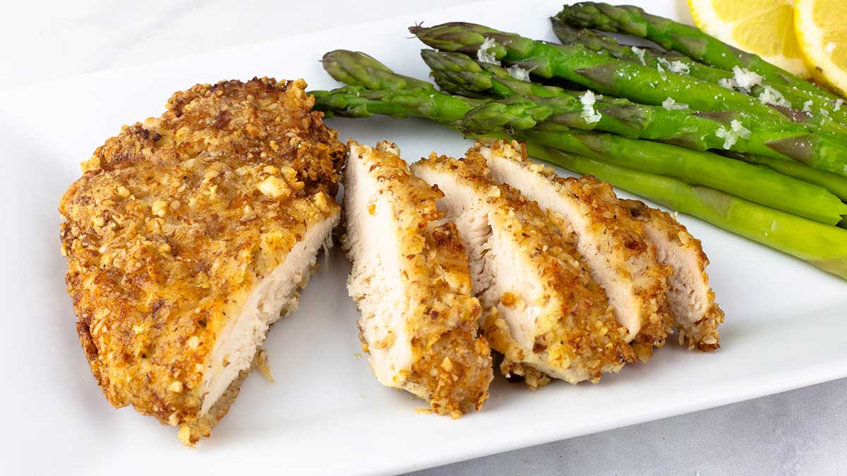 Parmesan crusted chicken sliced on a white plate with steamed asparagus.