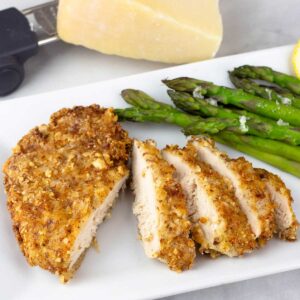 Parmesan crusted chicken sliced on a white plate with steamed asparagus.