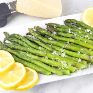 Steamed Asparagus on a white plate with lemon slices.
