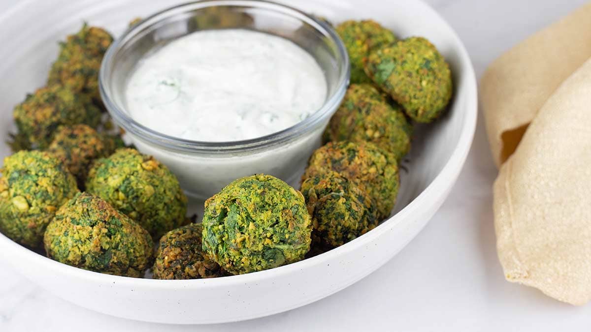 air fryer falafel in white bowl with a glass bowl of sauce in the center. 