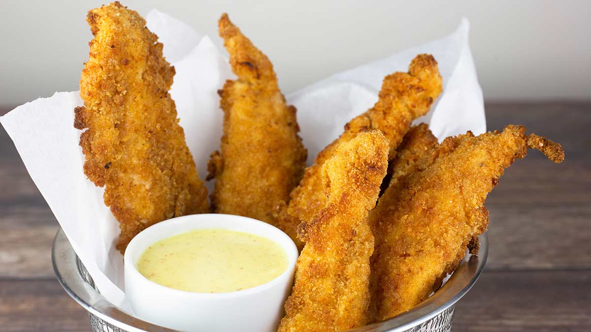 air fryer chicken strips in basket lined with parchment with a cup of honey mustard sauce.