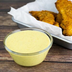 Honey Mustard Sauce in a glass bowl next to a tray of chicken tenders.