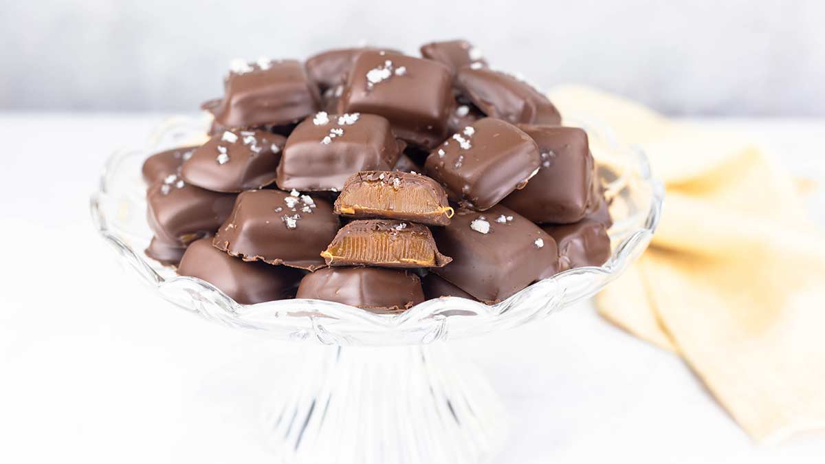 Caramels sitting on a glass platter stacked with a gold napkin beside them.