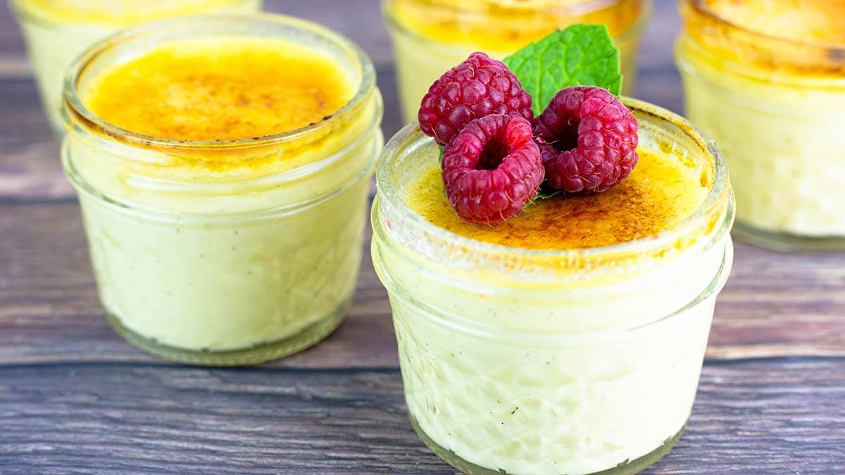 creme brulee in small jars topped with raspberries and mint garnish.