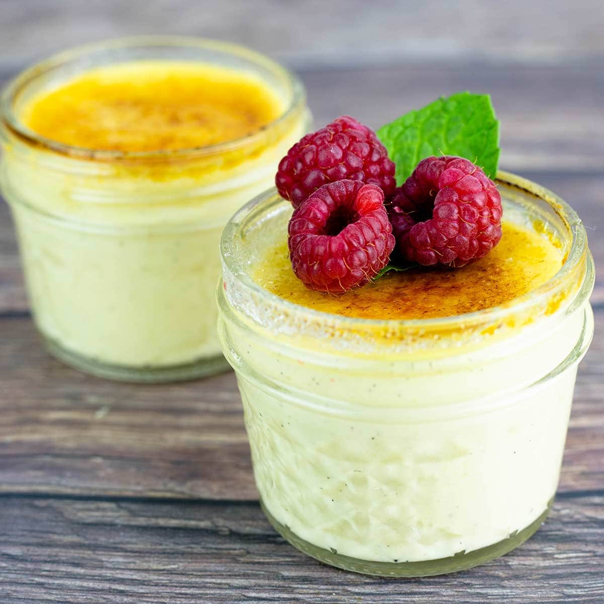creme brulee in small jars topped with raspberries and mint garnish.