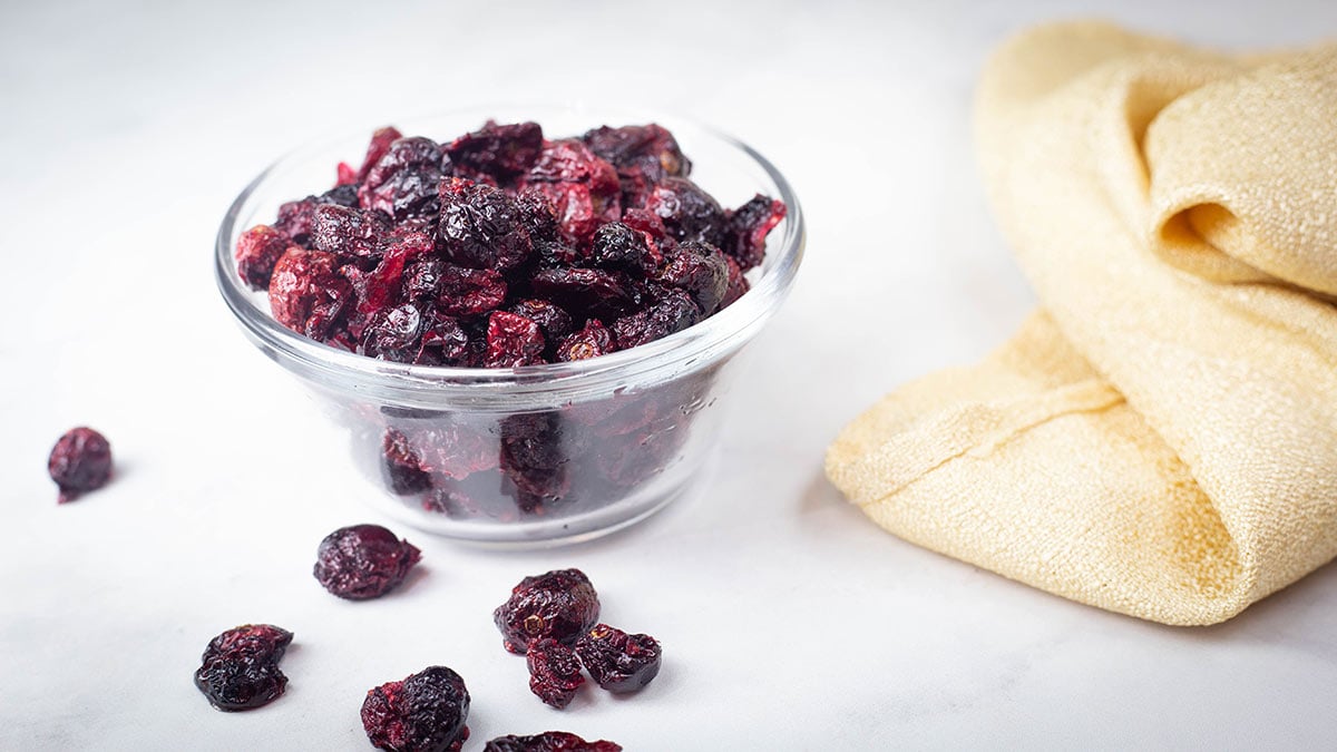 dehydrated cranberries in a glass bowl next to a gold napkin.