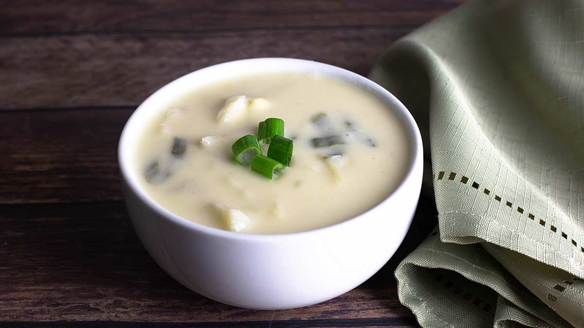 colcannon soup topped with green onions in a small white bowl next to a light green napkin.