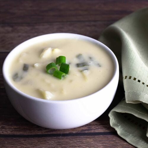 colcannon soup topped with green onions in a small white bowl next to a light green napkin.