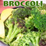 steam and crisped broccoli in black bowl with lemon garnish.