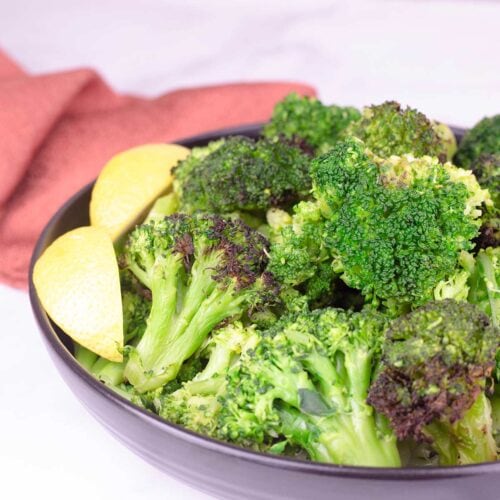 steam and crisped broccoli in black bowl with lemon garnish.