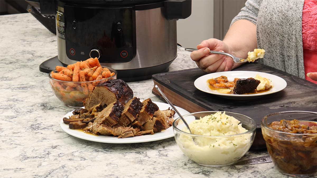 eye of round roast with mashed potatoes and carrots on a plate surrounded by the serving dishes.