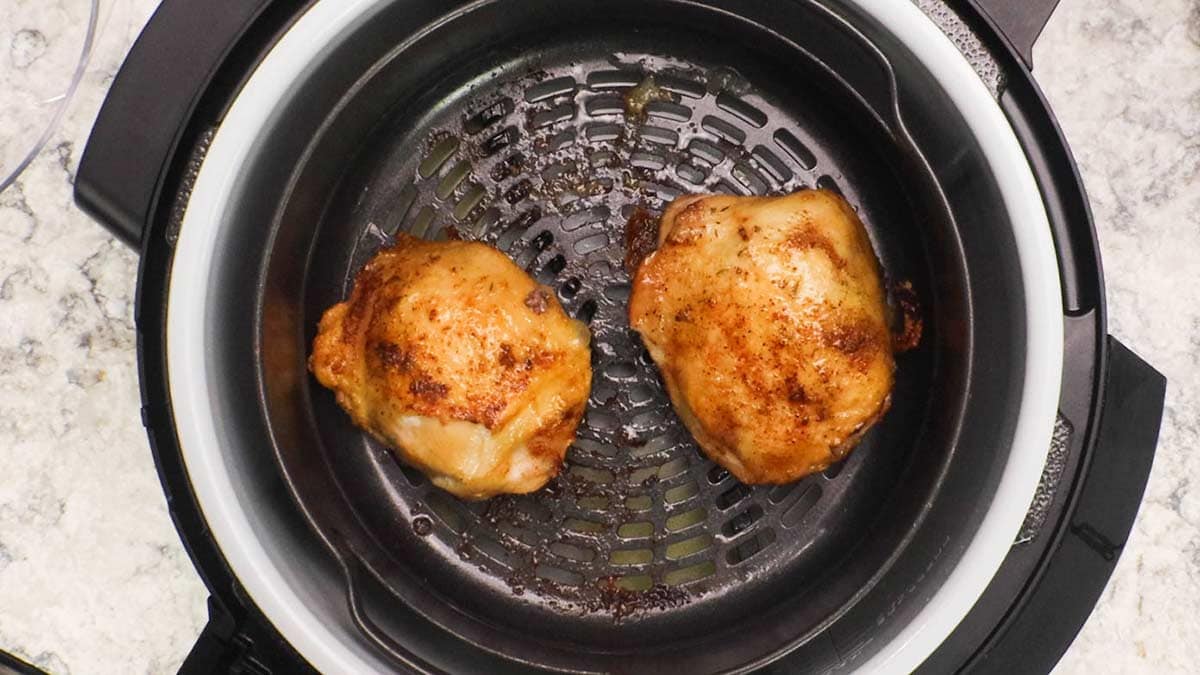 Cooked chicken thighs golden brown in air fryer basket.