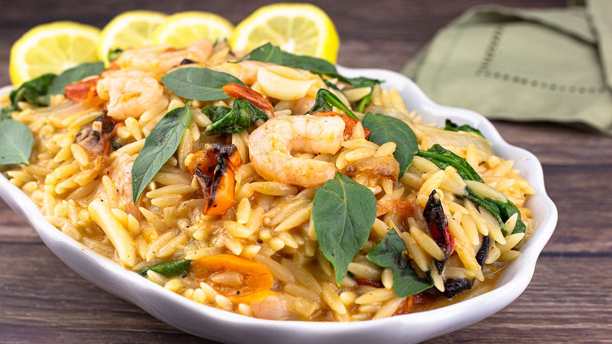 Lemon Orzo Pasta with vegetables and shrimp in a white serving bowl garnished with fresh basil leaves and lemon slices.