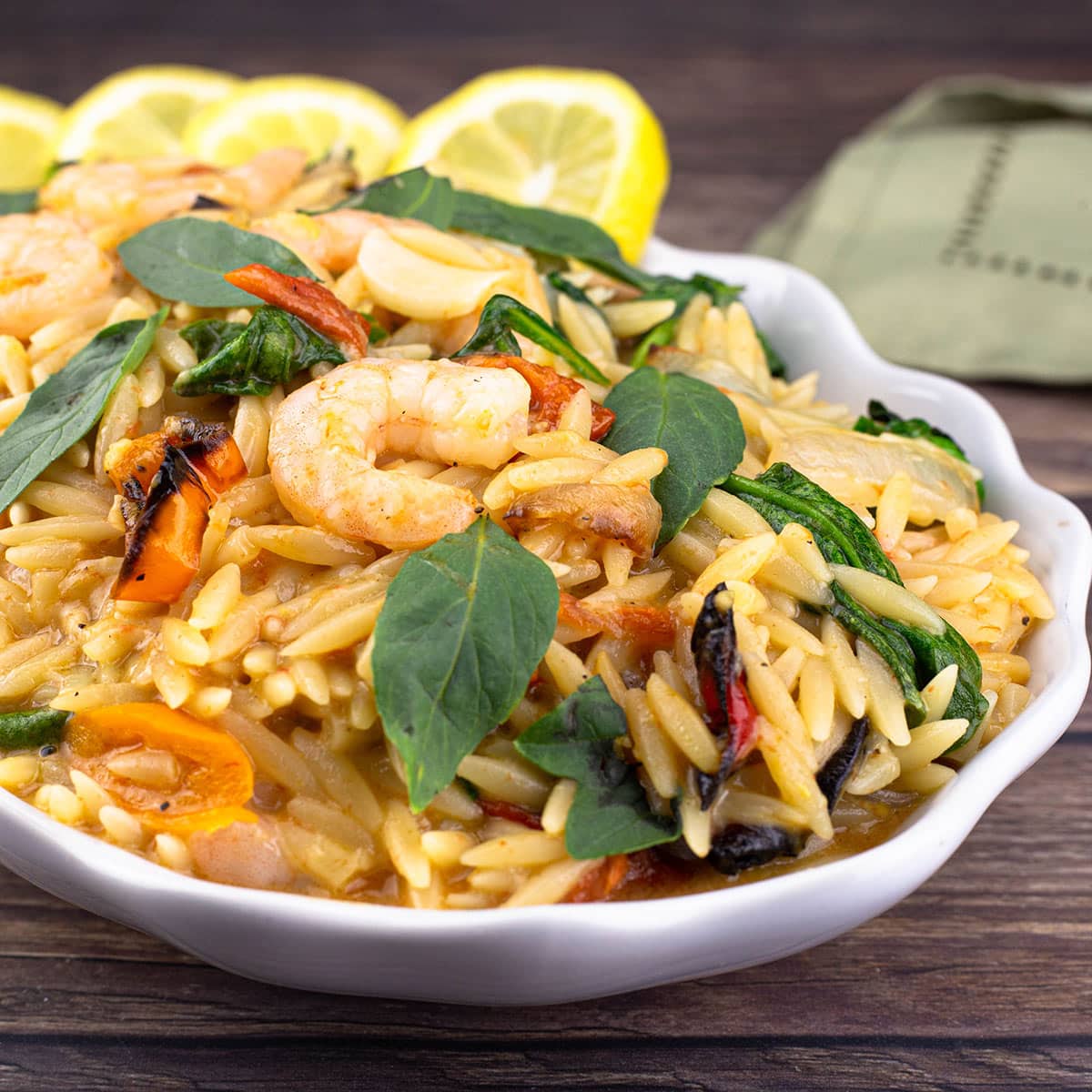 Lemon Orzo Pasta with vegetables and shrimp in a white serving bowl garnished with fresh basil leaves and lemon slices.