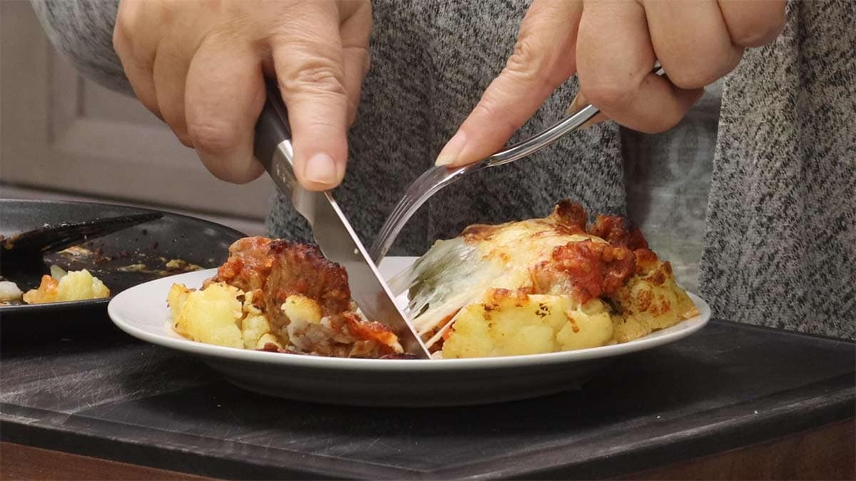 cauliflower parmesan on a plate being cut with a knife and fork.