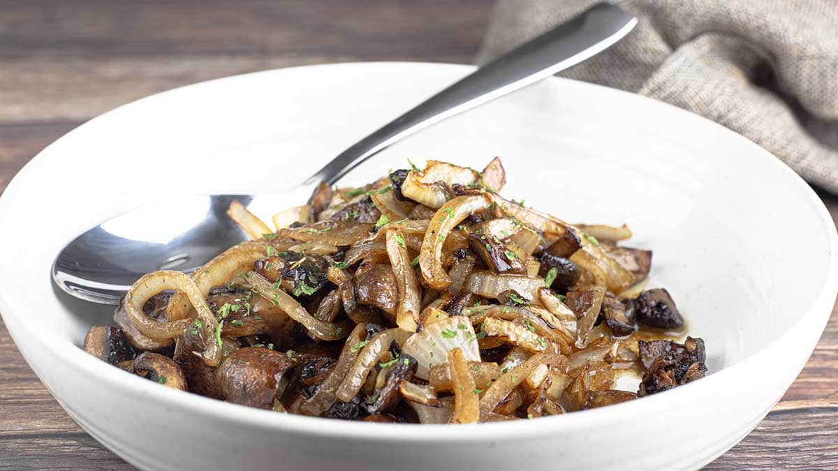 air fryer mushrooms and onions in white bowl with spoon and parsley garnish
