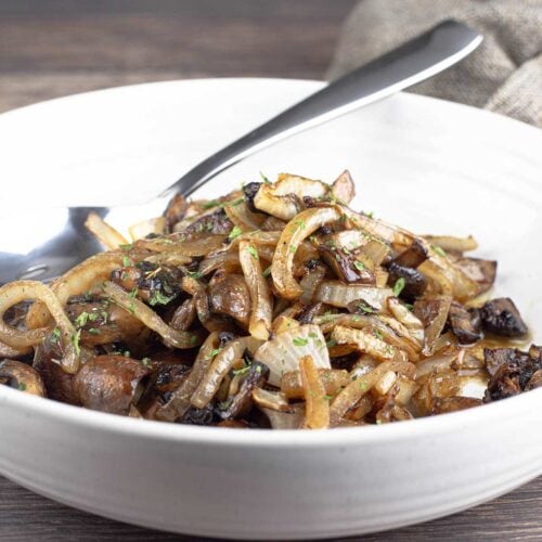 air fryer mushrooms and onions in white bowl with spoon and parsley garnish