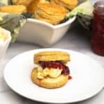 Air fryer scone on a white plate with clotted cream and strawberry jam.