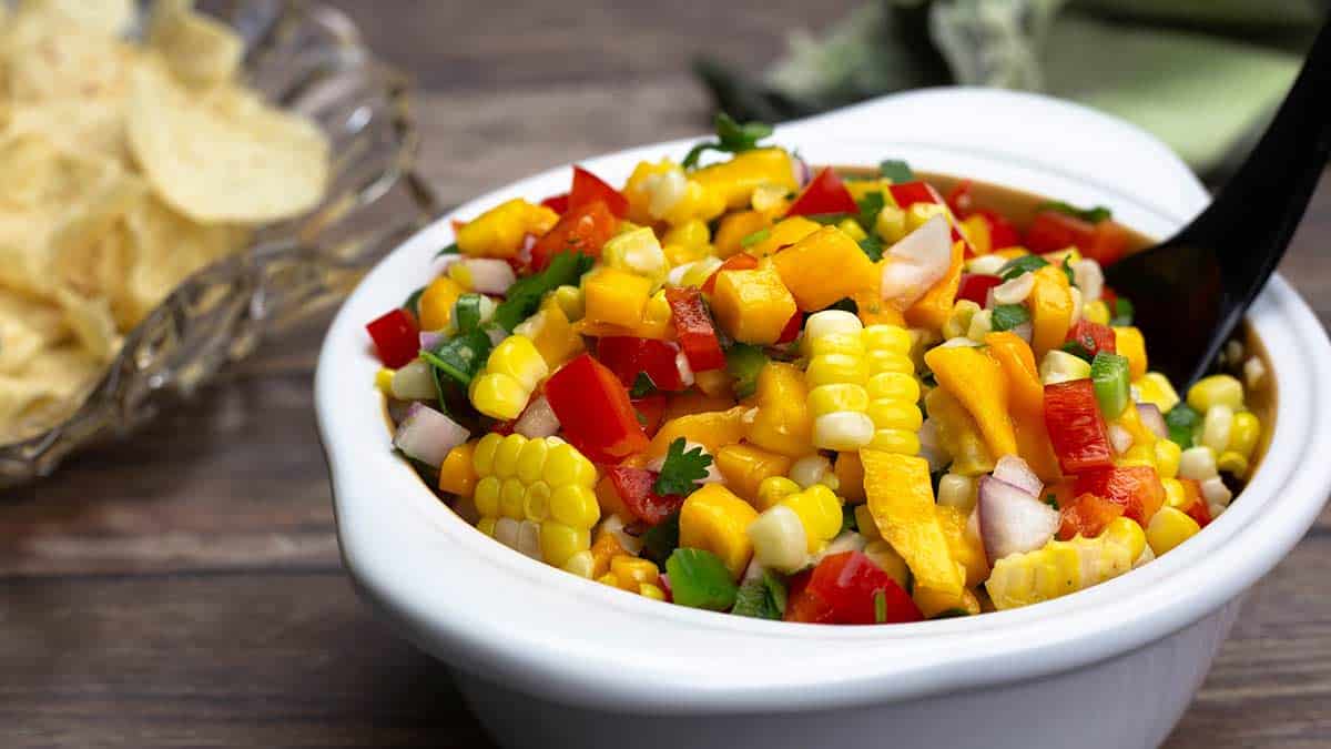 mango corn salsa in a white bowl next to tortilla chips.