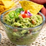 homemade guacamole in glass bowl with chips and fresh lime.