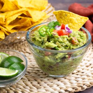 homemade guacamole in glass bowl with chips and fresh lime.