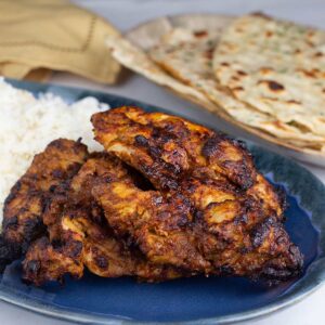 Chicken tandoori with basmati rice on a blue platter next to naan bread.