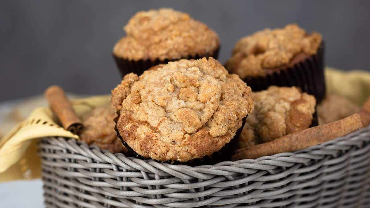 Cinnamon Raisin Muffins in a grey basket with a gold napkin and cinnamon sticks.