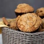 Cinnamon Raisin Muffins in a grey basket with a gold napkin and cinnamon sticks.