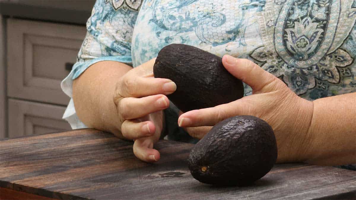 gently pressing on avocado to determine ripeness.
