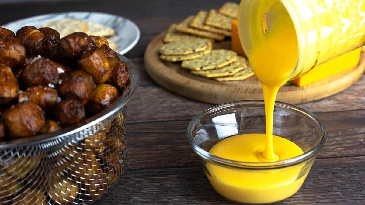 Pretzel cheese dip being poured into a bowl with air fryer pretzel bites next to the cheese.