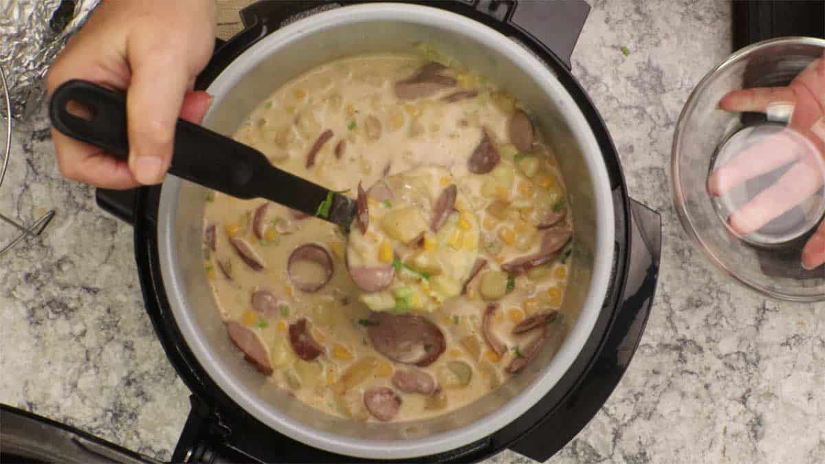 Ladling the sausage and corn chowder into a bowl. 