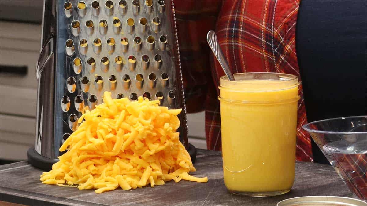 shredded cheddar in front of grater next to the cheese sauce.
