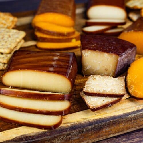 A variety of smoked cheeses on a cutting board next to crackers.