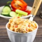 cheese spread in a white bowl with cut veggies in the background.