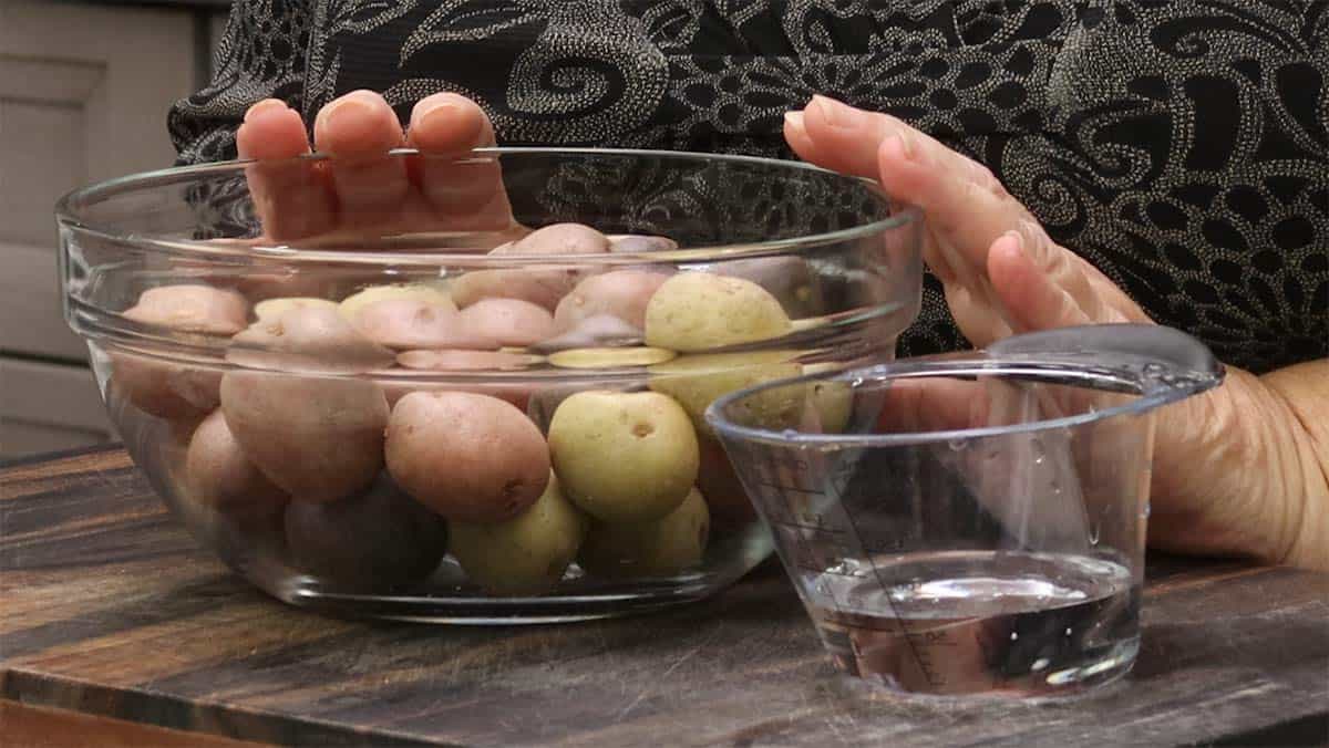 Small potatoes in a mixing bowl with a measuring cup of water beside them.