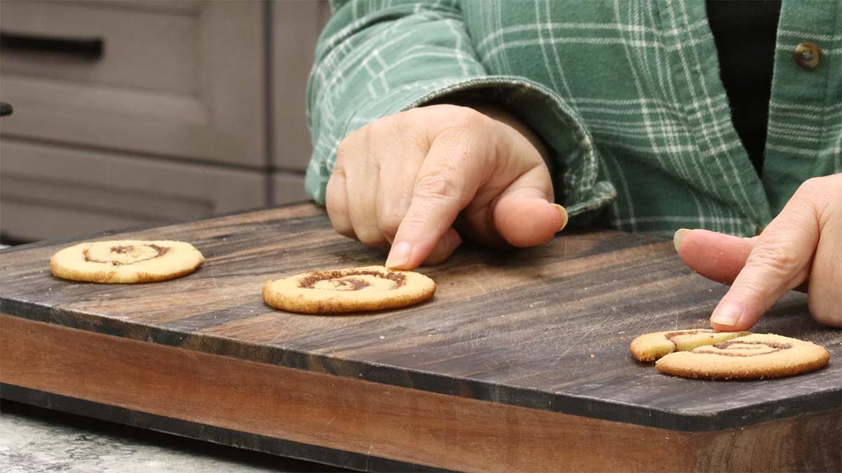three cinnamon roll cookies on cutting board that were baked different times.
