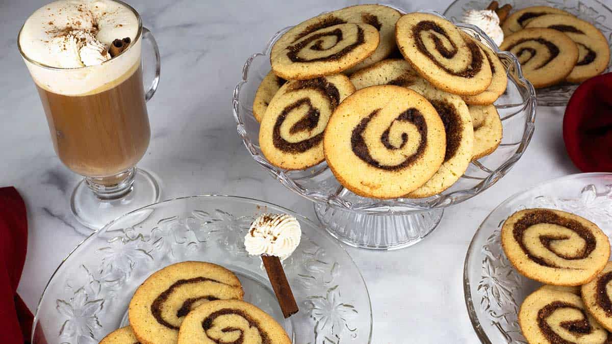 Cinnamon Roll Cookies on a round platter beside two plates of cookies and a cup of coffee. 