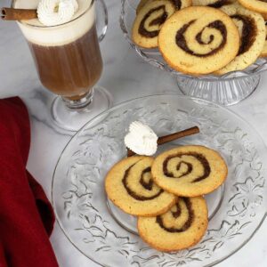 Cinnamon Roll Cookies on a round platter beside two plates of cookies and a cup of coffee.